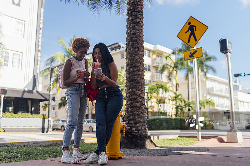 美国佛罗里达州迈阿密海滩，两个快乐的女性朋友带着手机和软饮料在城市里图片素材