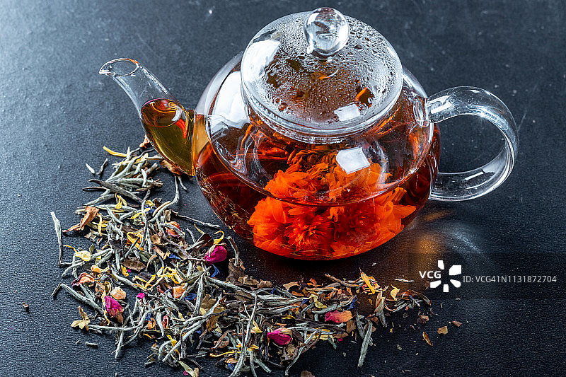 用玻璃茶壶泡茶，还有一朵盛开的大花。茶壶与异国情调的绿茶球盛开花，干茶和玫瑰花蕾图片素材