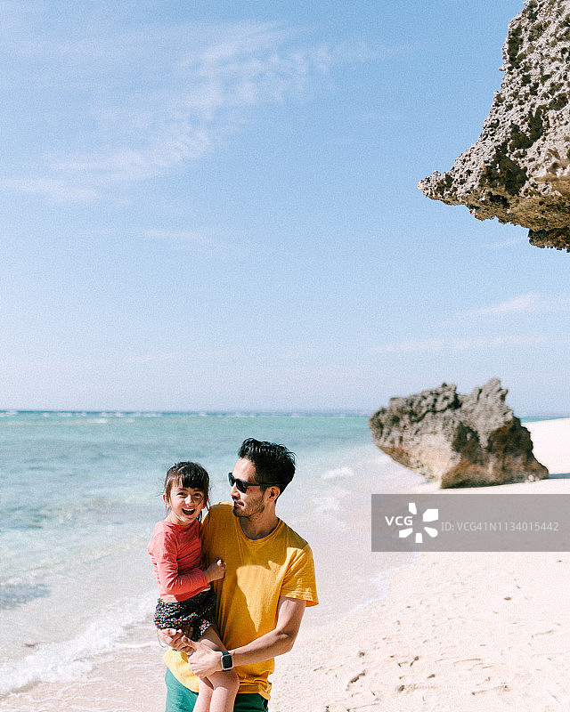 父亲抱着他可爱的小女孩在热带海滩，冲绳，日本图片素材
