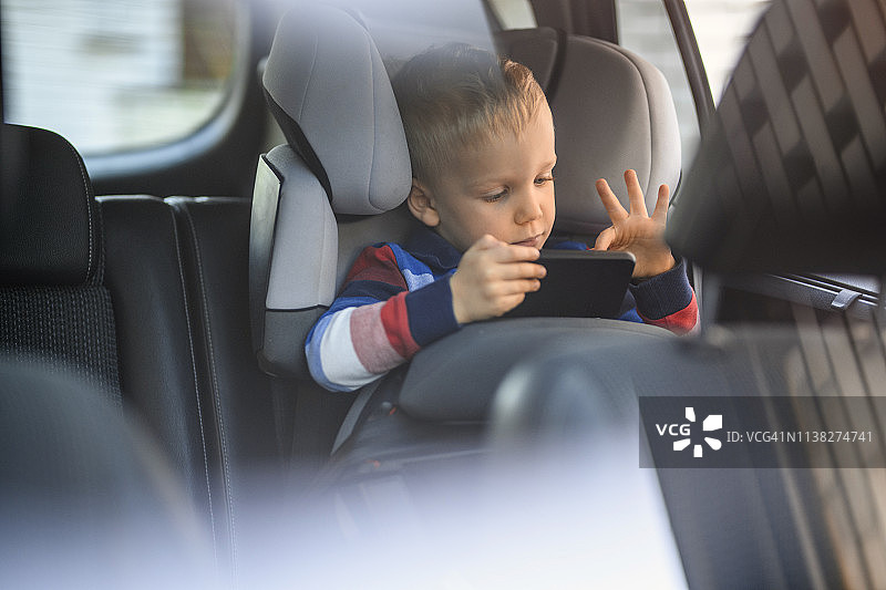 一个小男孩在汽车安全座椅上使用手机图片素材