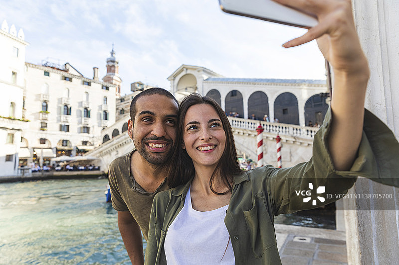 在意大利威尼斯，一对夫妇享受着这座城市，并以里亚托桥为背景自拍图片素材