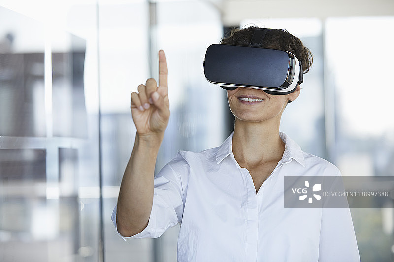 女商人戴着虚拟现实眼镜在办公室举起手指图片素材