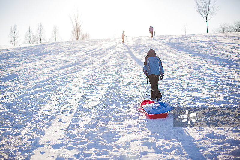 一个男孩拉着雪橇上山图片素材