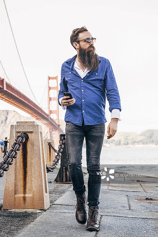 美国加州旧金山，一名留胡子的男子在金门大桥检查智能手机图片素材