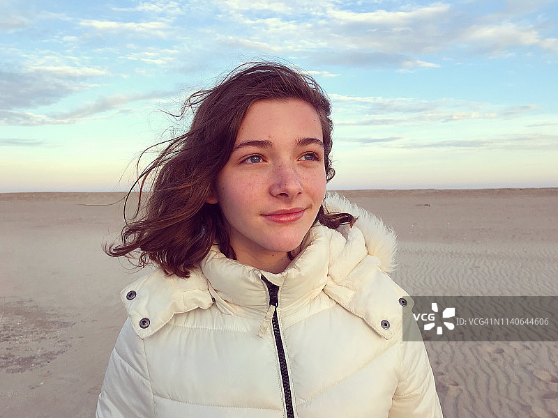 一个十几岁的女孩站在冬天的海滩上的肖像图片素材
