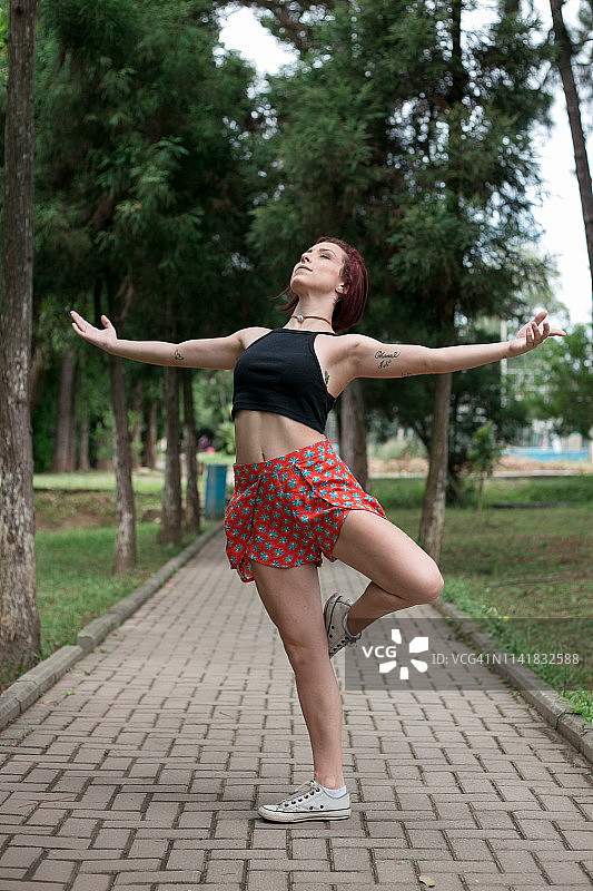 在一个阳光明媚的日子里，快乐的红发女孩在巴西的一个绿色公园跳舞图片素材