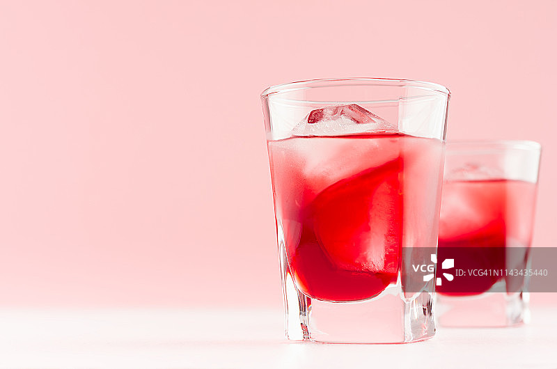 新鲜的冷红色夏季水果鸡尾酒与冰块在优雅的现代厨房室内轻柔和的粉色白色木板。图片素材