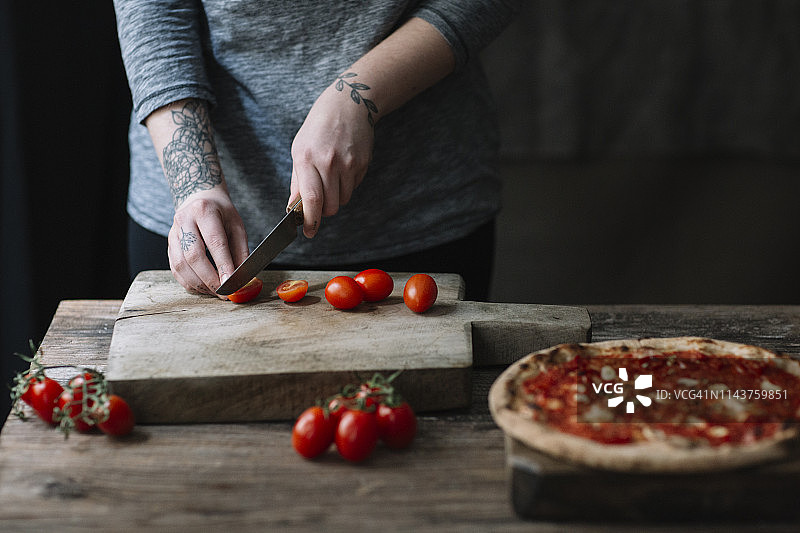 年轻女子准备披萨，在切菜板上切西红柿图片素材