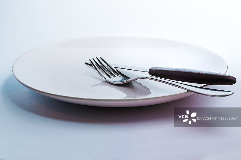 一个简单的白色空锅盘，在白色统一的背景下进餐，配有优雅的钢餐具，如刀叉图片素材