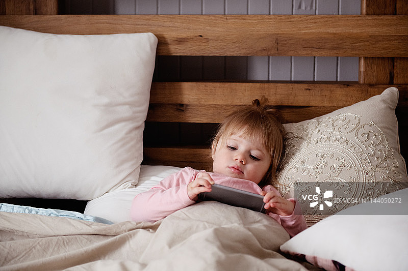 可爱的小女孩在床上玩手机图片素材