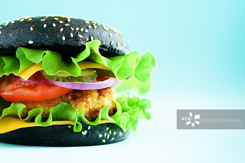 美味的黑色汉堡与牛肉，奶酪，生菜，洋葱，西红柿在蓝色背景的宏观视图。关闭横幅。不健康的饮食概念和复制空间图片素材
