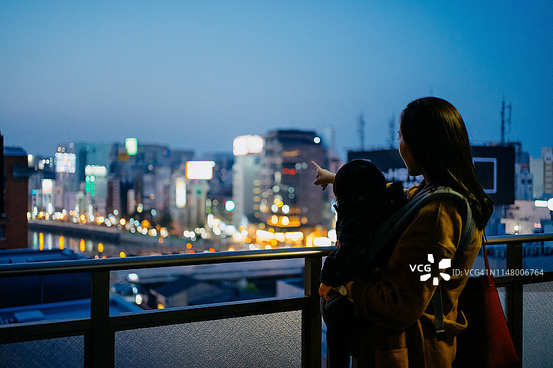 年轻的母亲抱着小女儿从阳台上欣赏美丽的城市夜景图片素材