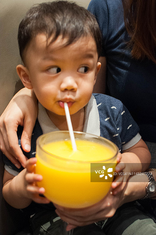 一个小男孩正在用纸吸管喝芒果奶昔图片素材