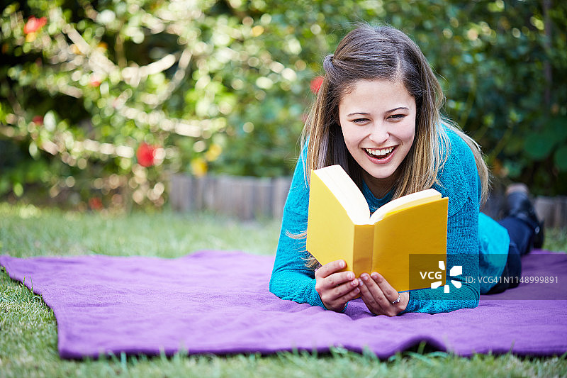 漂亮的黑发女人微笑着看书，她正在她的花园里图片素材