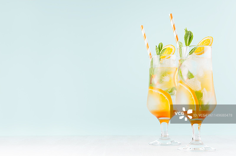 热带清爽水果饮料与切片橘子，绿色薄荷，冰，吸管在柔软的轻白色木板和柔和的绿色内饰。图片素材