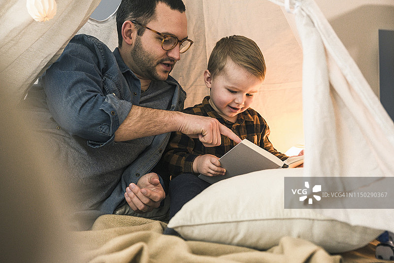 父亲和儿子一起在家里的帐篷里看书图片素材