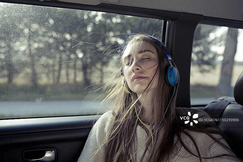 年轻女子，头发被风吹乱，戴着耳机坐在车里图片素材