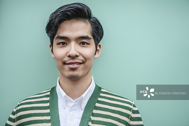 肖像迷人的年轻日本男子在绿色和白色条纹开襟羊毛衫图片素材