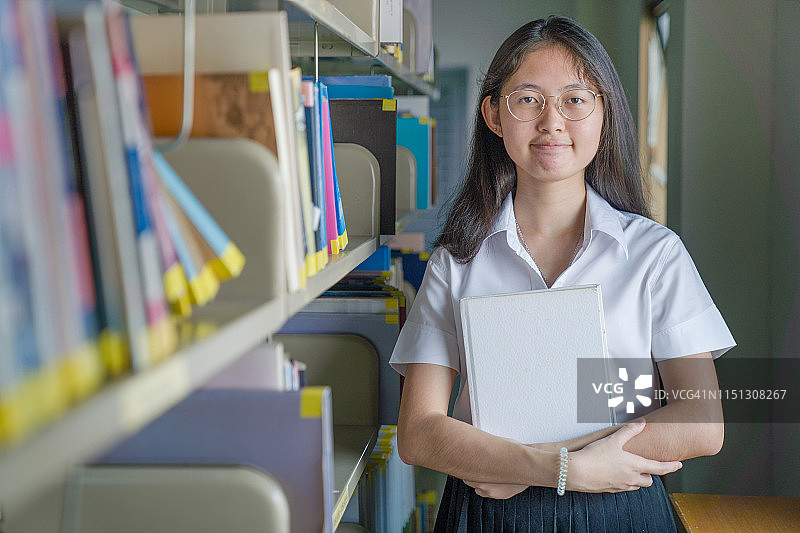 亚洲大学生女孩读书和工作用笔记本电脑和智能手机做她的家庭作业在公共图书馆图片素材