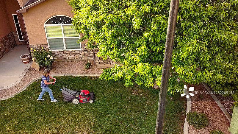 一个中年妇女在修剪草坪，享受仲春天气的无人机视频剪辑图片素材