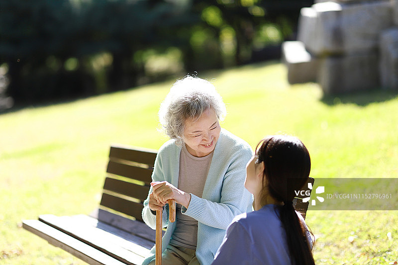 护士协助年长妇女在公园长凳上图片素材