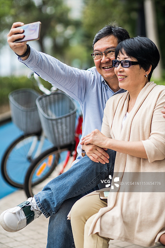 一对成熟的亚洲夫妇坐在长椅上自拍。图片素材