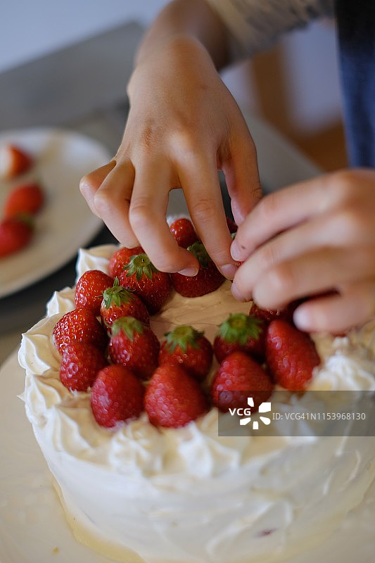 孩子在厨房装饰草莓蛋糕，近距离拍摄图片素材