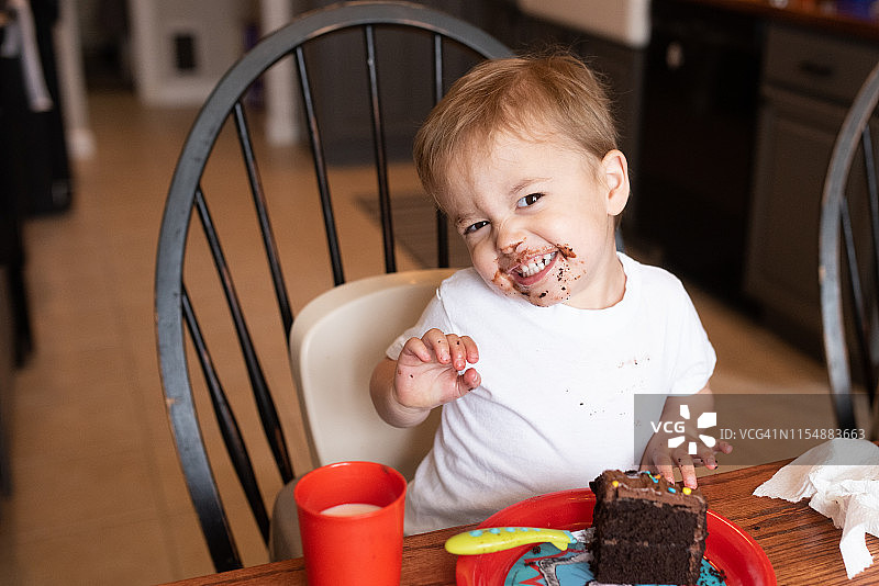 在他的生日派对上，3岁的金发男孩脸上满是巧克力蛋糕，笑得很开心图片素材