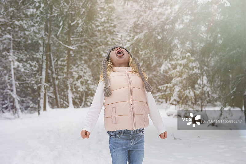 冬天，一个年轻的女孩站在森林小径上，用舌头捕捉雪花。图片素材