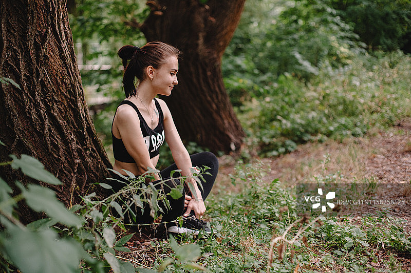 一个女人坐在公园的树干边练习瑜伽图片素材