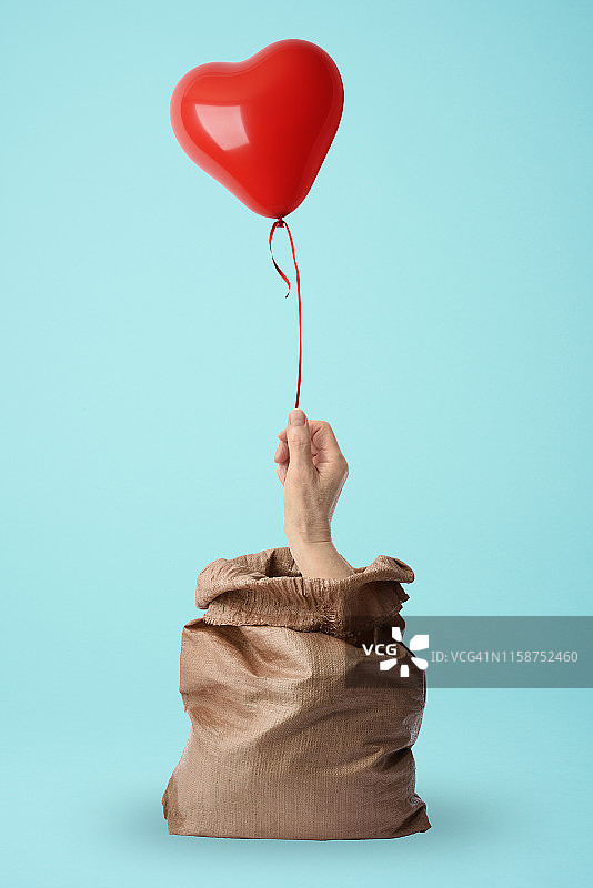 一只手从麻袋里拿着一个红色的心形气球图片素材