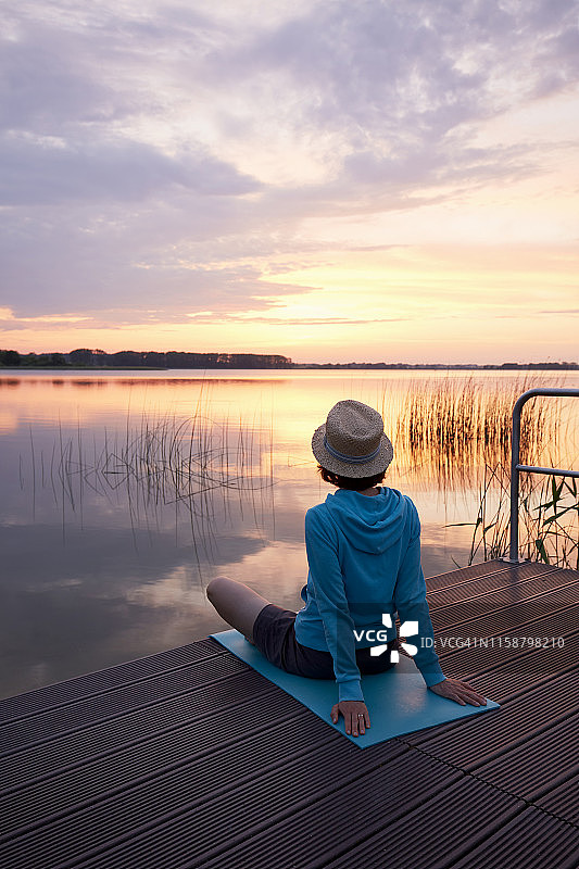日落时分，一个女人坐在田园诗般的湖边的码头上图片素材