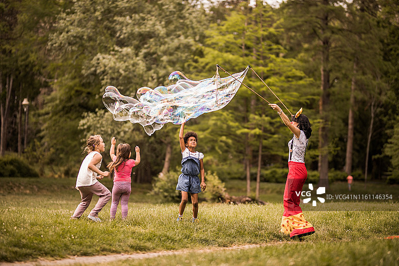 无忧无虑的女孩们在公园里玩由艺术家制作的彩虹泡泡。图片素材
