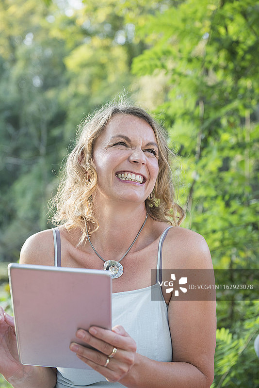 美丽的微笑女人在大自然中使用数字平板电脑，德国图片素材
