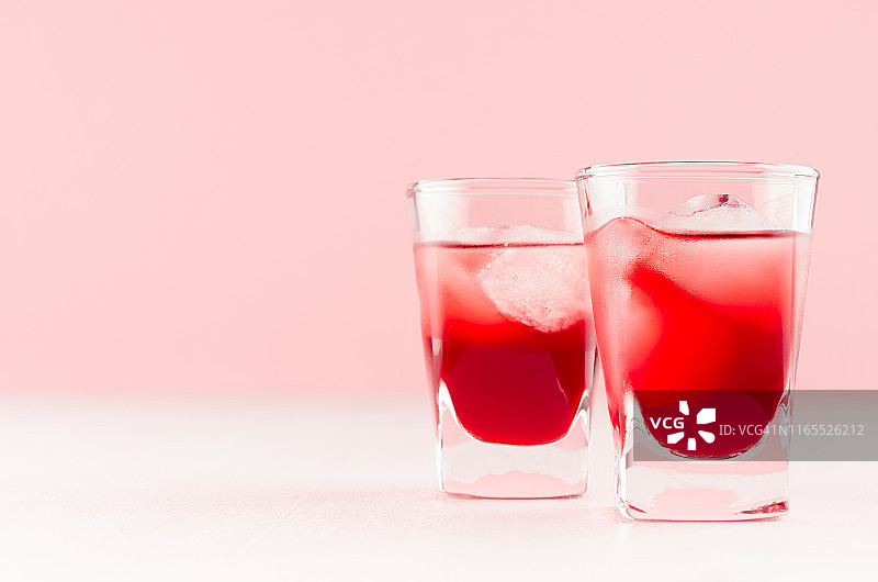 多汁的红草莓热带冷鸡尾酒与冰块在两个湿的小酒杯，在白色木板和浅粉背景，复制空间。图片素材