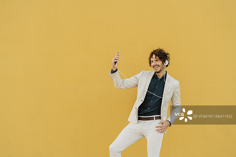 商人在黄色墙壁前跳舞，用耳机和智能手机听音乐图片素材