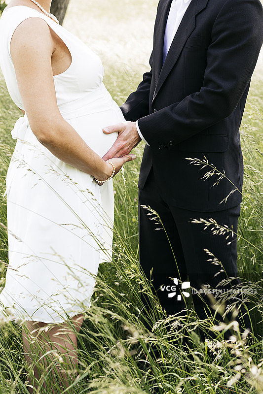 怀孕的新娘和她的丈夫抱着小宝宝在草地上图片素材