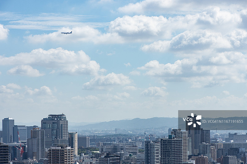 夏天的云朵和飞机在大阪的城市建筑上飞行图片素材