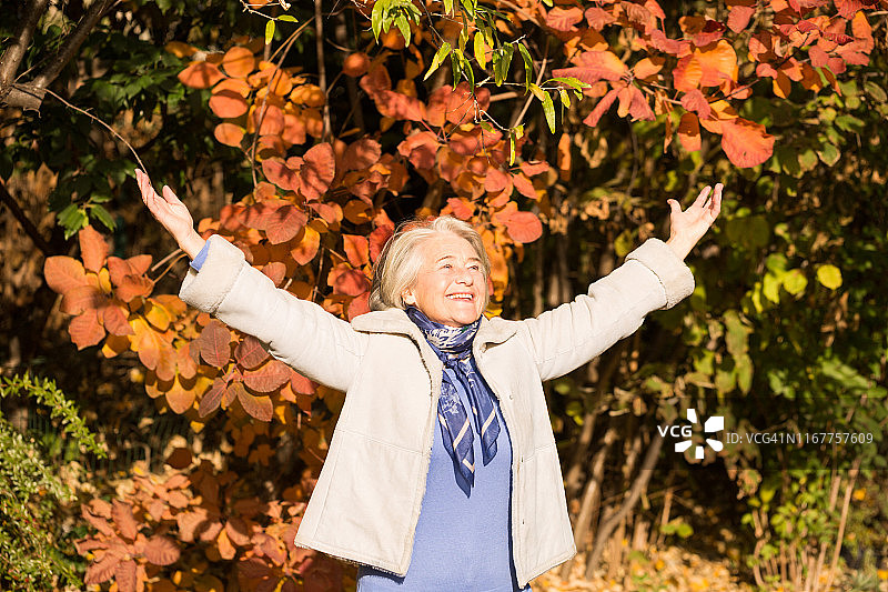 一个美丽的微笑奶奶的手臂在空气中的秋天的颜色。图片素材