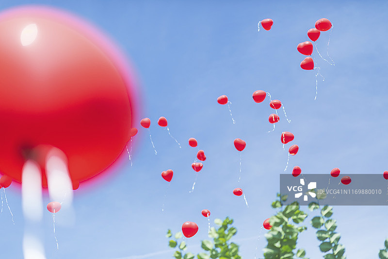 红色心形气球映衬着蓝色的天空。图片素材