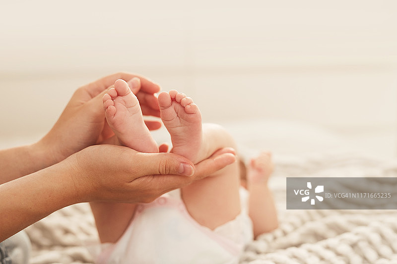 年轻母亲的双手抱着躺在床上的新生儿的脚图片素材