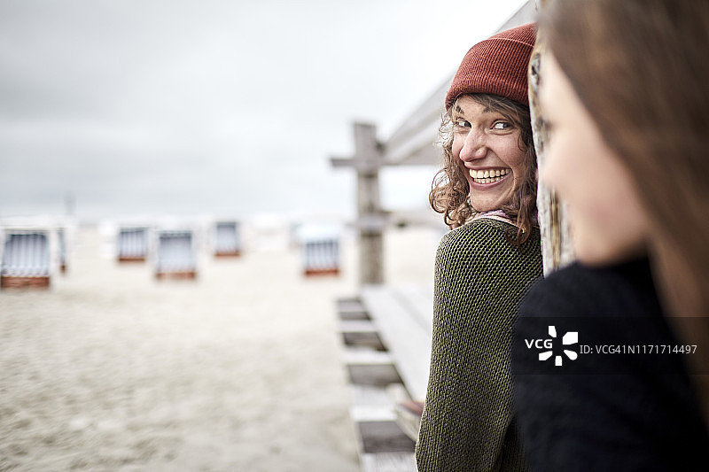 快乐的年轻女人看着海滩上的木板路上的女孩图片素材