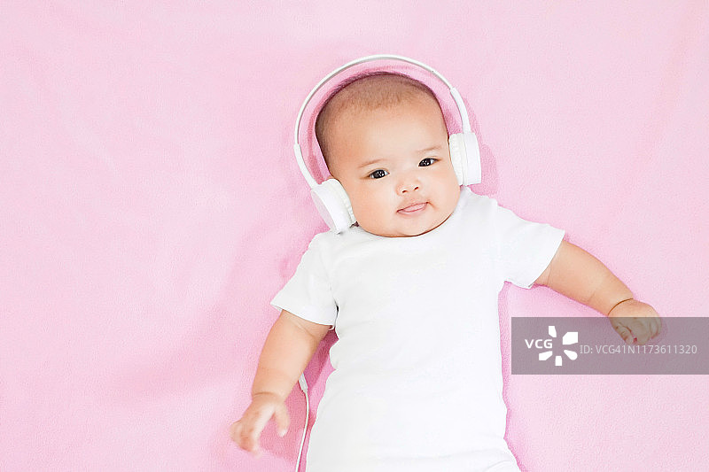 亚洲女婴戴着白色耳机，白色衬衫，粉红色背景图片素材