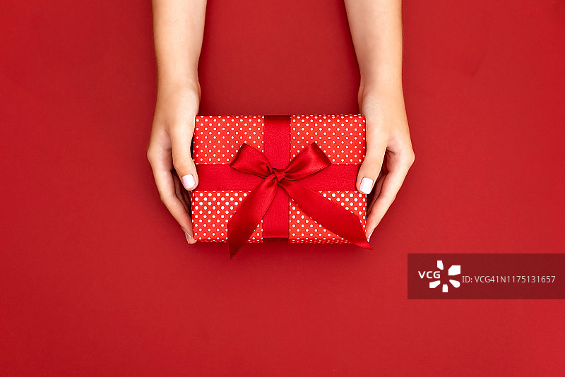女性手握礼物与红色的蝴蝶结在白色的乡村闪闪发光的背景。节日背景:生日，情人节，圣诞节，新年。平躺图片素材