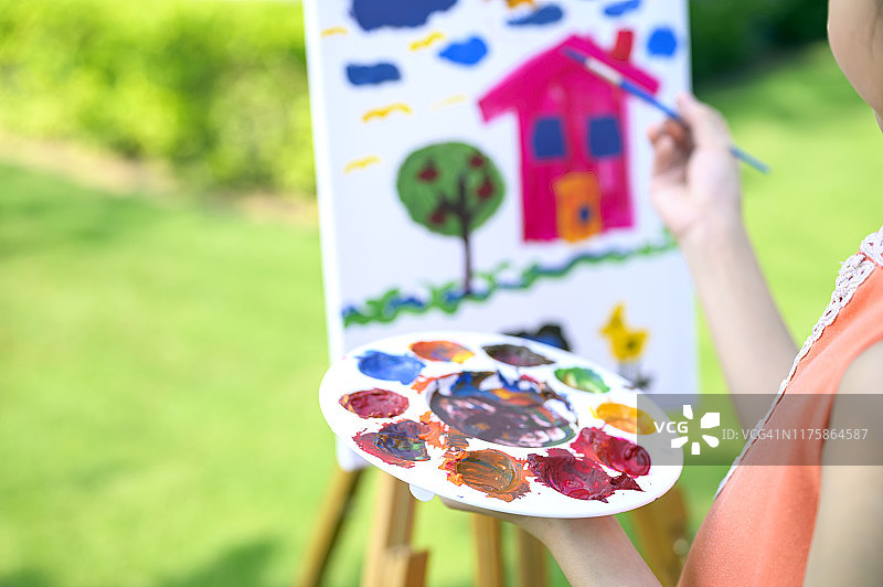 特写的年轻亚洲天才女孩享受绘画的房子画在画布上。图片素材