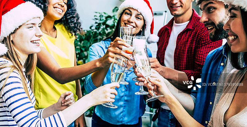 干杯!一群年轻人庆祝新年前夕，并与香槟碰杯，在五彩缤纷的背景下彼此微笑和大笑图片素材