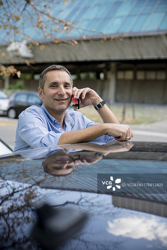 英俊的商人站在他的车旁用智能手机聊天图片素材
