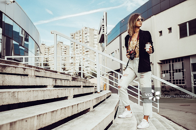 女人拿着相机和咖啡走在城市的街道上图片素材