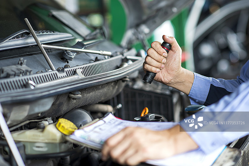 汽车修理工拿着手电筒检查汽车引擎。图片素材