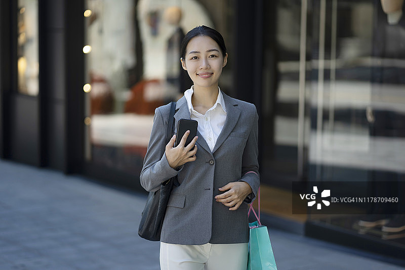 一名年轻女子在城市街道上提着购物袋的肖像图片素材